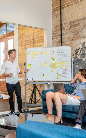 three-men-sitting-while-using-laptops-and-watching-man-beside-whiteboard.jpg three men sitting while using laptops and watching man beside whiteboard